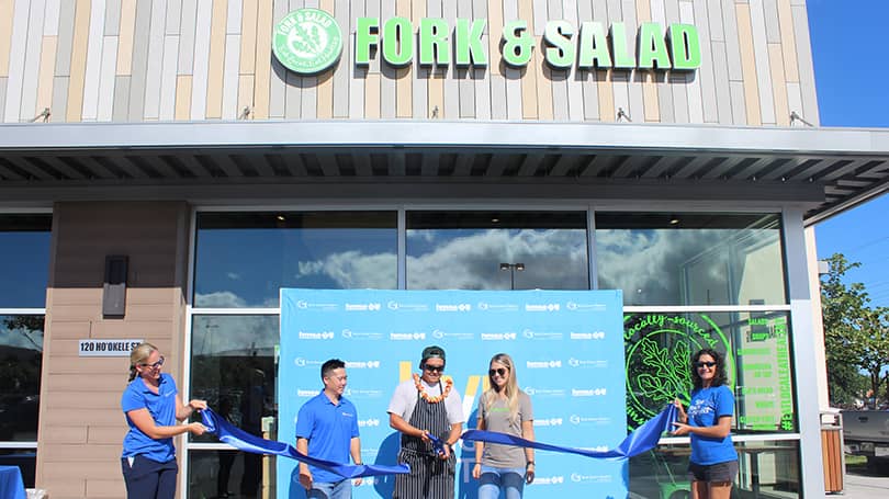 Restaurant employees cutting a celebratory ribbon outside of their restaurant